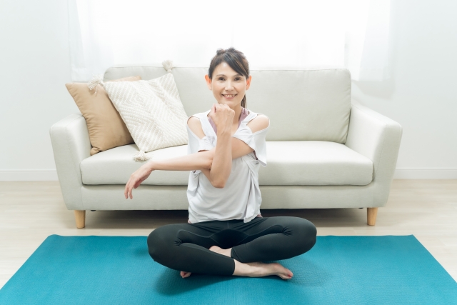 屋内で上半身（両腕、肩回り）のストレッチを行う女性