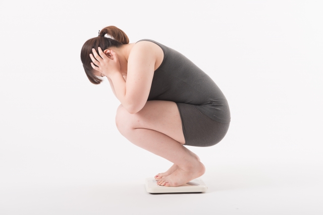 体重計の上で頭を抱えている・悩んでいるダイエット中の女性