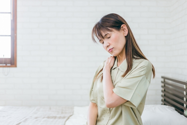 ベッドの上で首から肩を押さえている女性（体の痛み、寝つきの悪さ、不眠など）