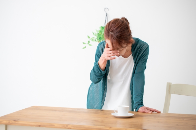 頭を押さえてかがむ女性（頭痛、体調不良、めまい、ストレスなど）